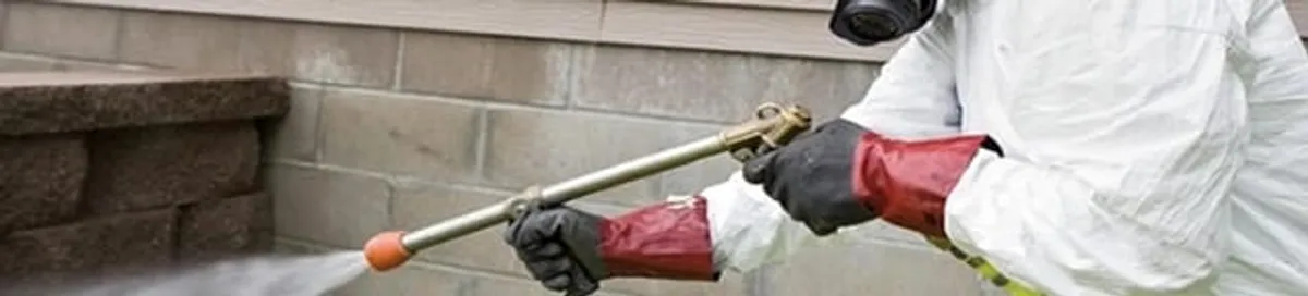 Pest control technician applying exterior insect treatment along a home foundation in Fargo, ND