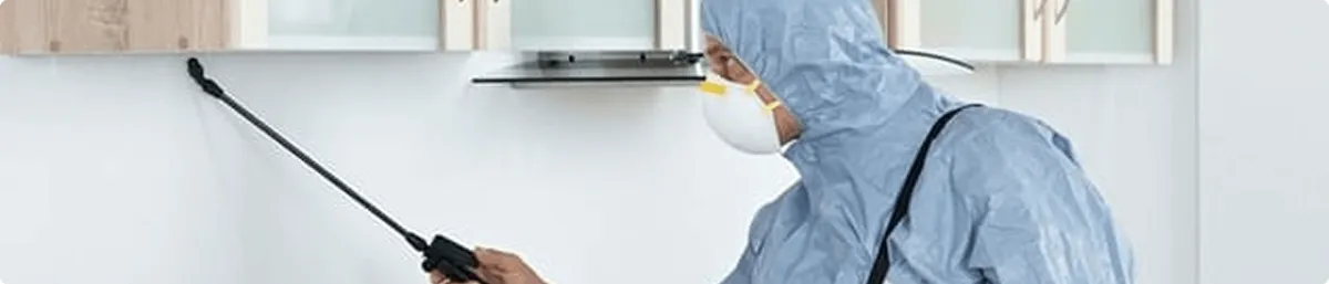 Pest control technician spraying along baseboards for indoor pest treatment in Fargo, ND