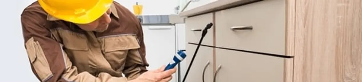 Roach exterminator applying treatment under kitchen cabinets in Fargo, ND