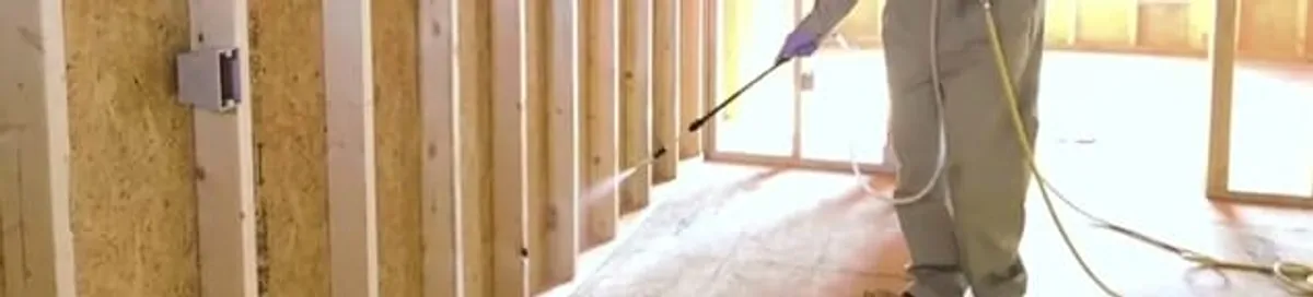 Termite treatment technician applying spray along framing and unfinished walls in Fargo, ND